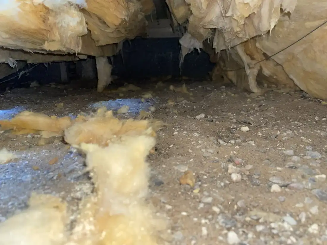 Mineraluld der hænger ned fra gulvkonstruktionen i en krybekælder